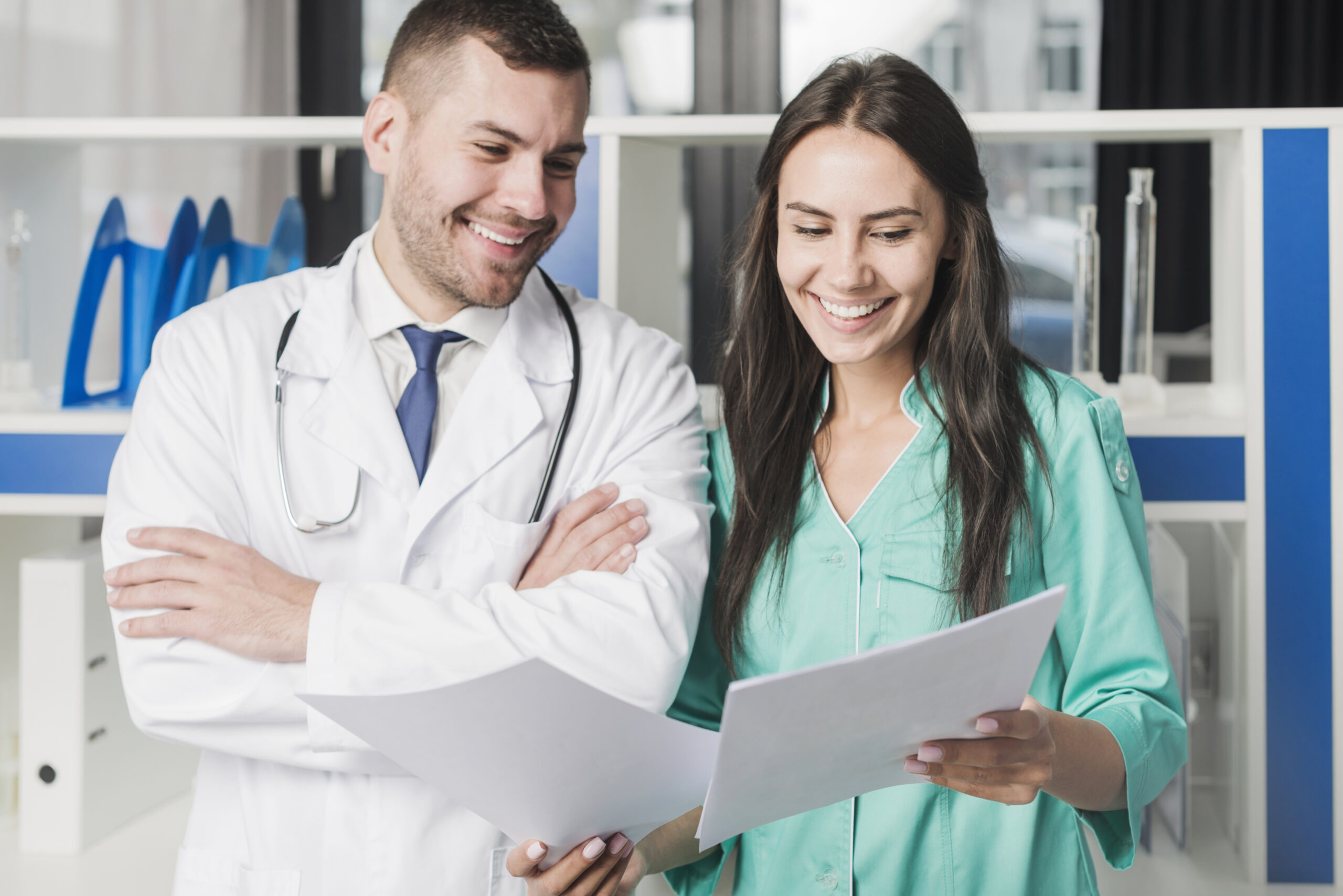 beautiful radiologist holding clipboard while standing near assistant and looking at camera e1697536007180